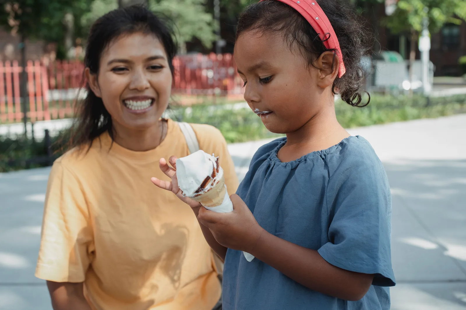 A mother and daughter laughing on a neighborhood sidewalk